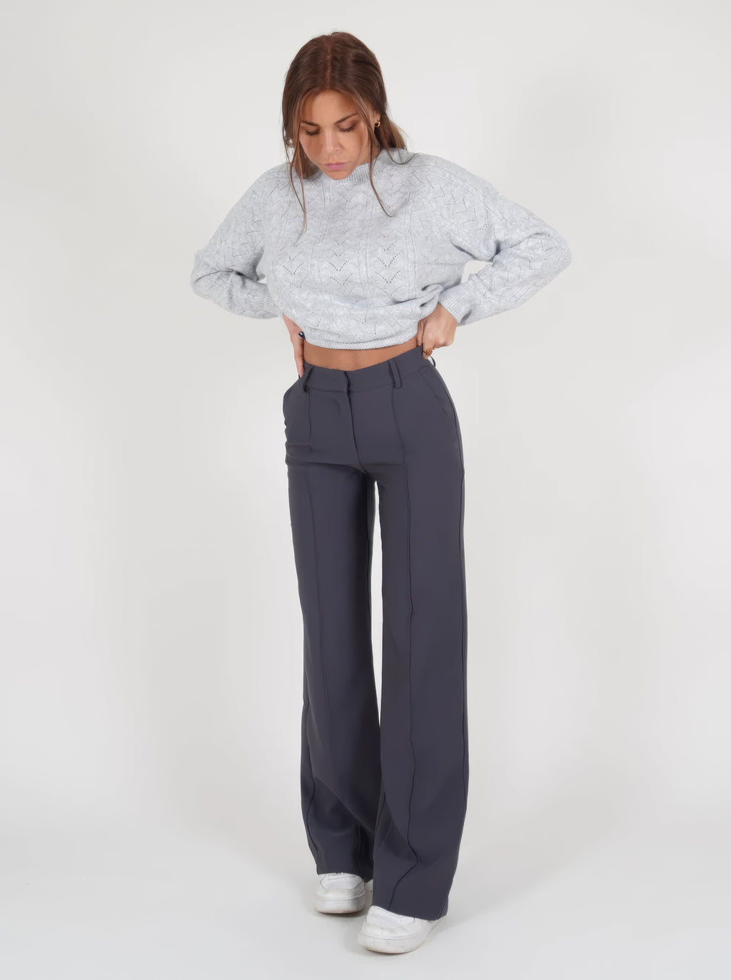 Grey trousers viewed from the front with hands near the waistband.