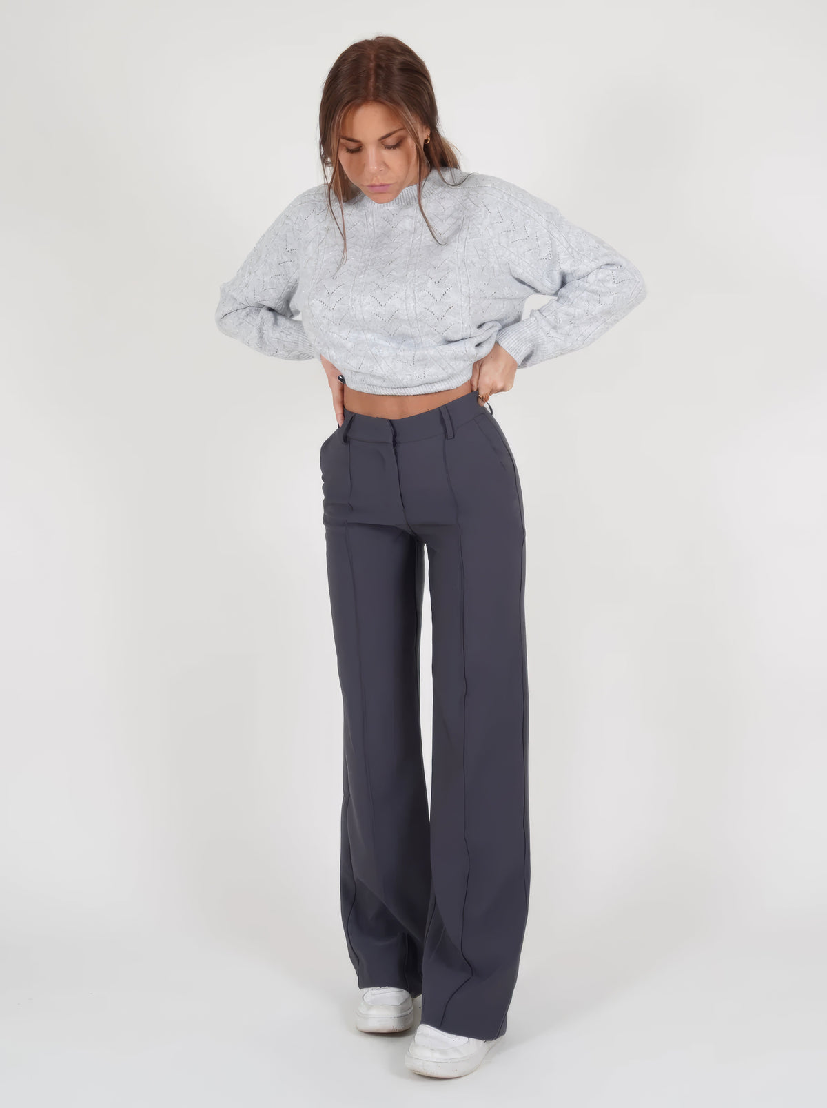 Grey trousers viewed from the front with hands near the waistband.