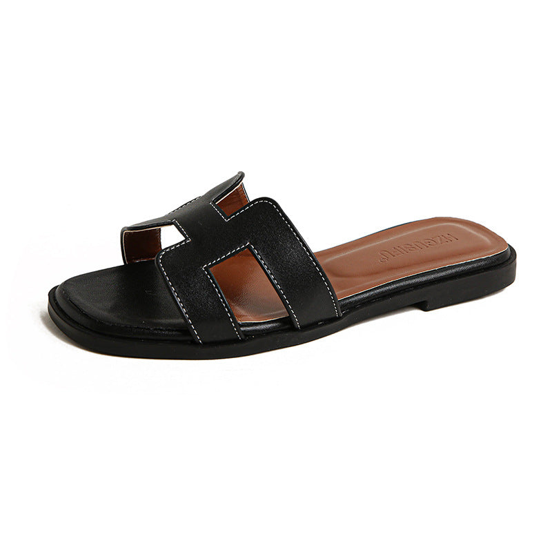 Black flat slide sandal with contrast stitching and a brown footbed.