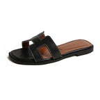 Black flat slide sandal with contrast stitching and a brown footbed.