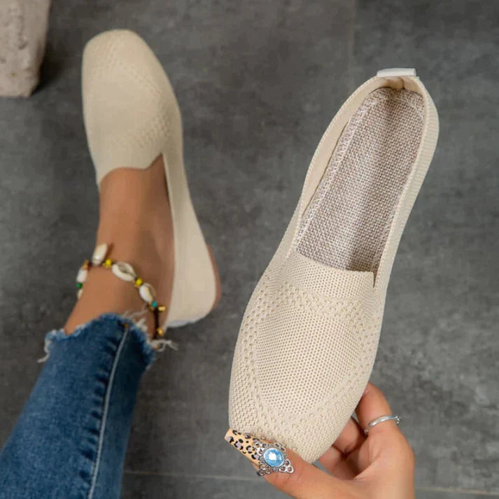 Beige textured slip-on flats, with one shoe held to show the opening and insole.