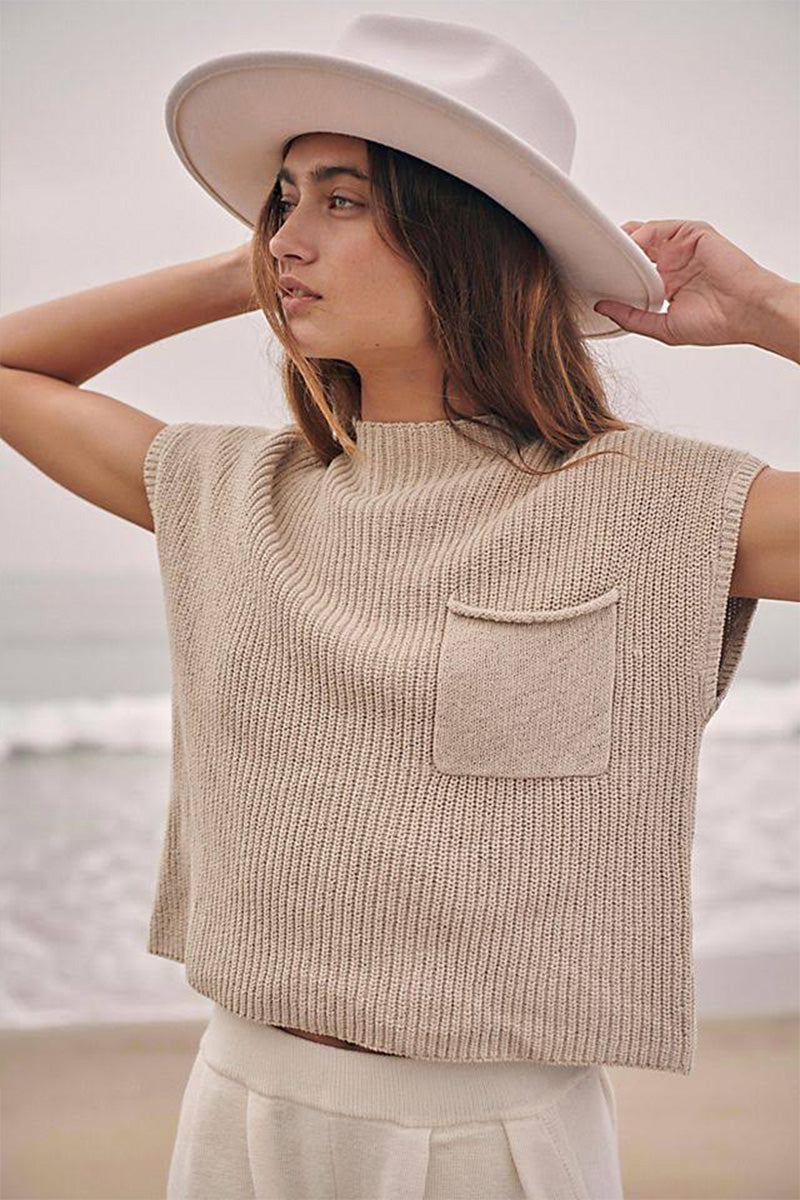 Beige short-sleeve knit top with a chest pocket worn above cream trousers.