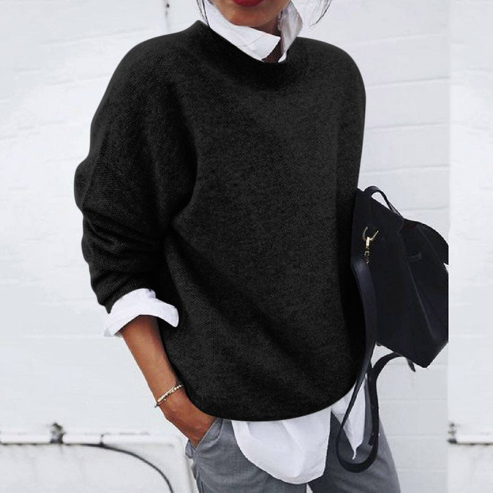 Black jumper layered over a white shirt, with a black bag beside it.