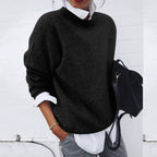Black jumper layered over a white shirt, with a black bag beside it.