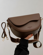 Coffee-brown bag with a wide adjustable strap and curved flap.