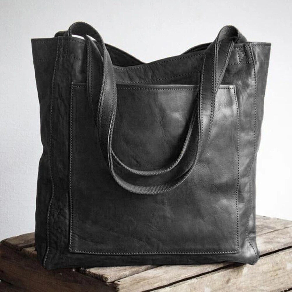 Black tote bag with two handles and a stitched front pocket.