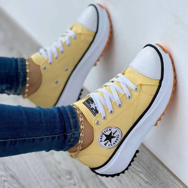 Yellow trainers with white laces and rounded white toe caps.