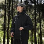 Black jacket worn outdoors with a hat and walking pole.