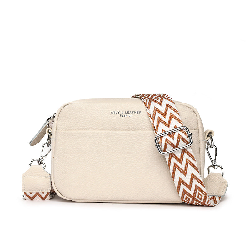 Beige shoulder bag with a wide patterned strap and front pocket.