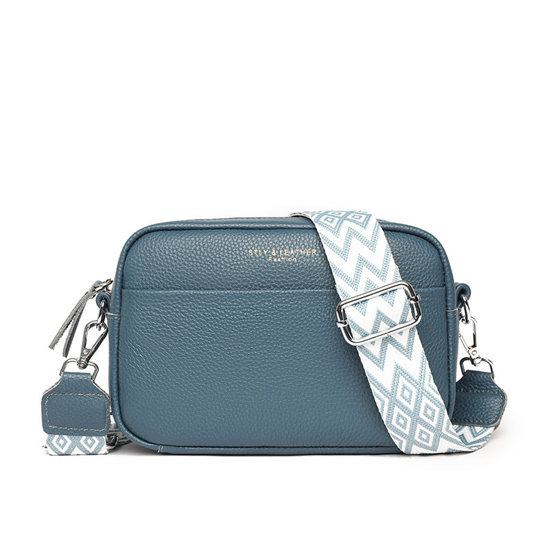 Blue shoulder bag with a patterned strap and front pocket.