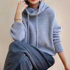 Grey jumper worn seated, showing its long cuffed sleeves.