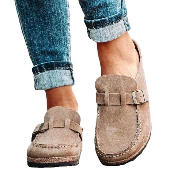 Close-up of tan clogs with stitched toes and metal buckles.