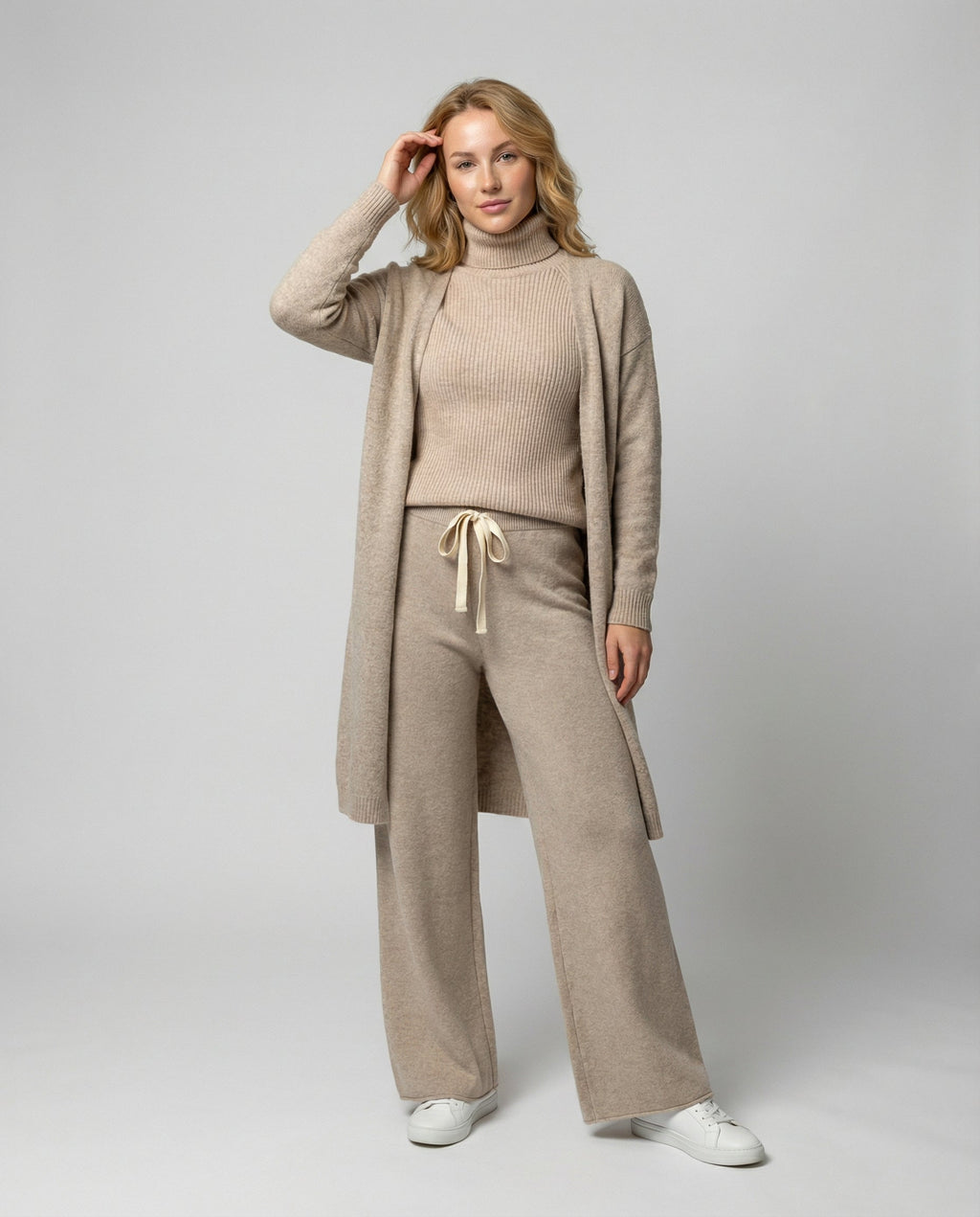 Woman wearing a beige roll-neck jumper, wide-leg drawstring trousers and a long open knit jacket.