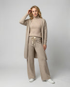 Woman wearing a beige roll-neck jumper, wide-leg drawstring trousers and a long open knit jacket.