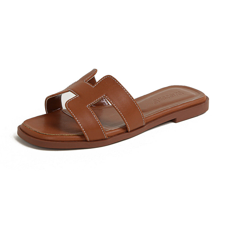 Brown flat slide sandal with a cut-out strap, pale stitching and embossed insole lettering.