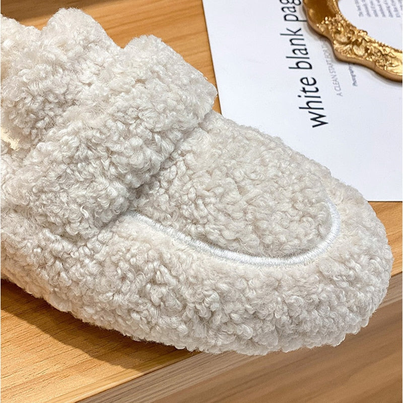 Close view of a cream plush slipper showing its curly texture and curved toe seam.