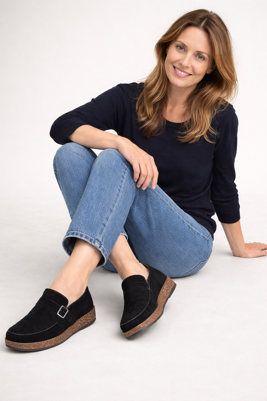 Black buckle clogs worn with blue jeans while seated.