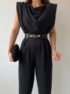 Black round-neck jumpsuit with a draped front and decorative belt.