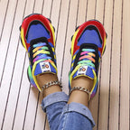 Blue and red sneakers with multicoloured laces and rainbow soles, shown from above.