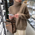 Brown roll-neck sweater worn by a woman holding a phone beside a handbag.
