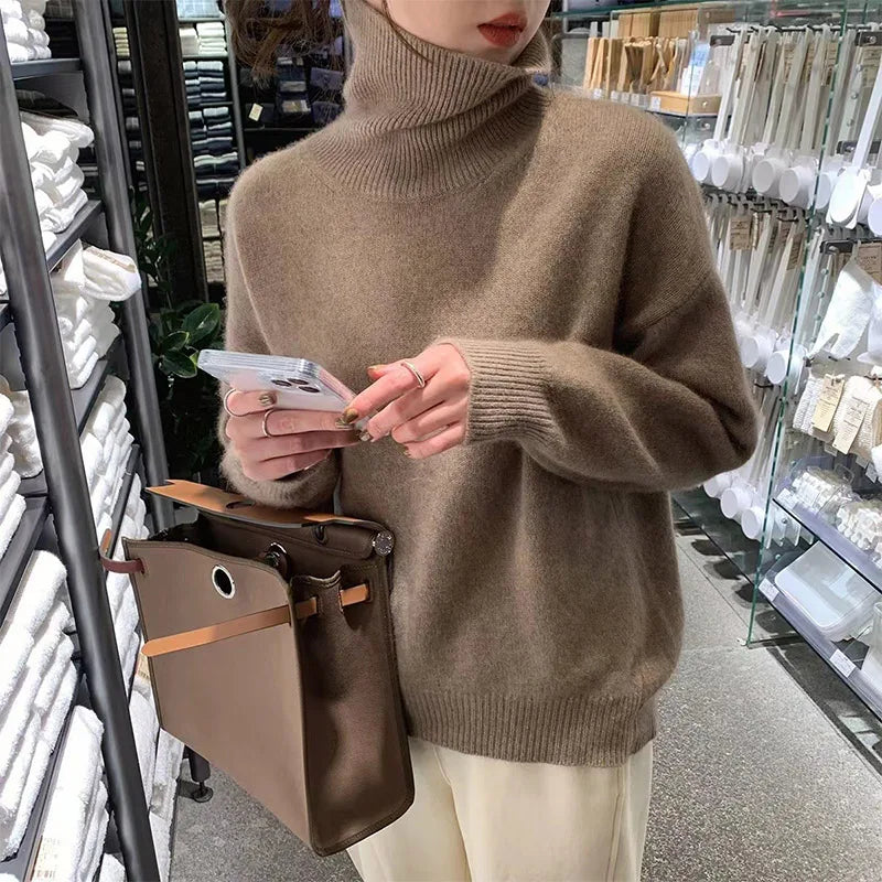 Brown roll-neck sweater worn by a woman holding a phone beside a handbag.
