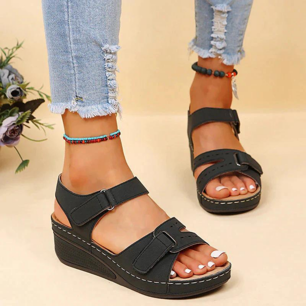 Black sandals showing the wedge sole and contrast stitching.