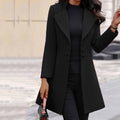 Black longline coat with shiny buttons and a wide collar, worn with dark trousers.