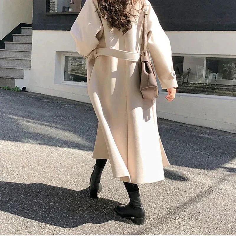 Long beige coat worn with a matching waist belt and black boots.