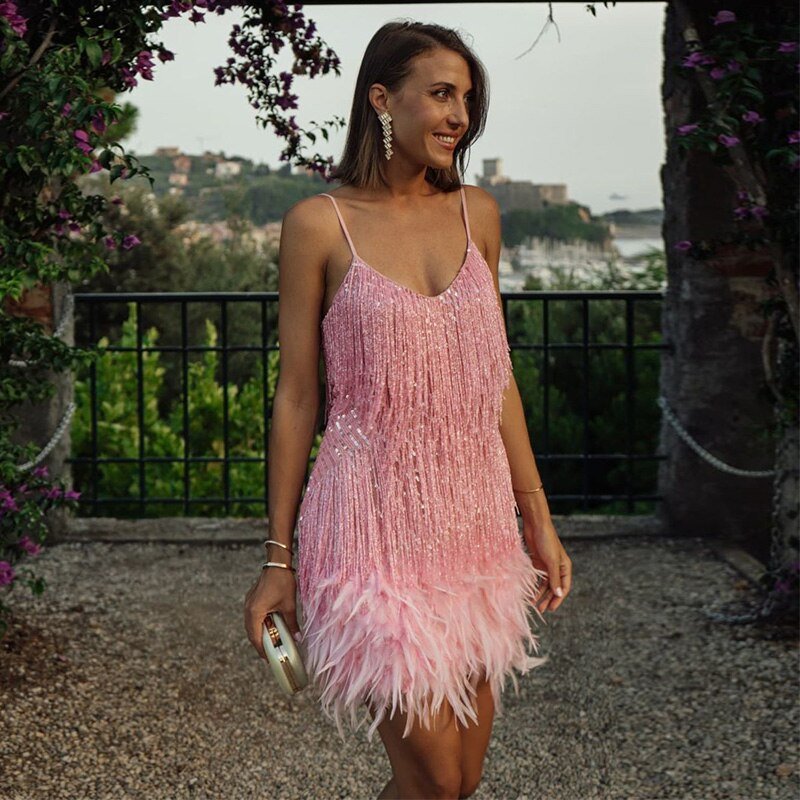 Pink spaghetti-strap dress with long fringe and pale feather trim, photographed beside a railing.