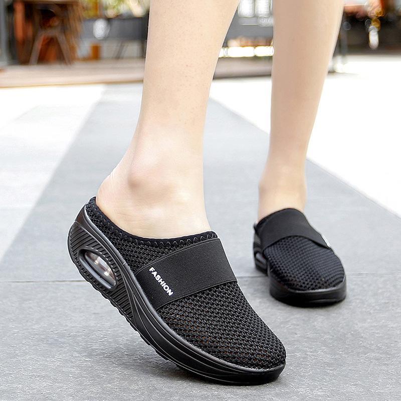 Black mesh mules worn on a pavement, with FASHION lettering on the front bands.