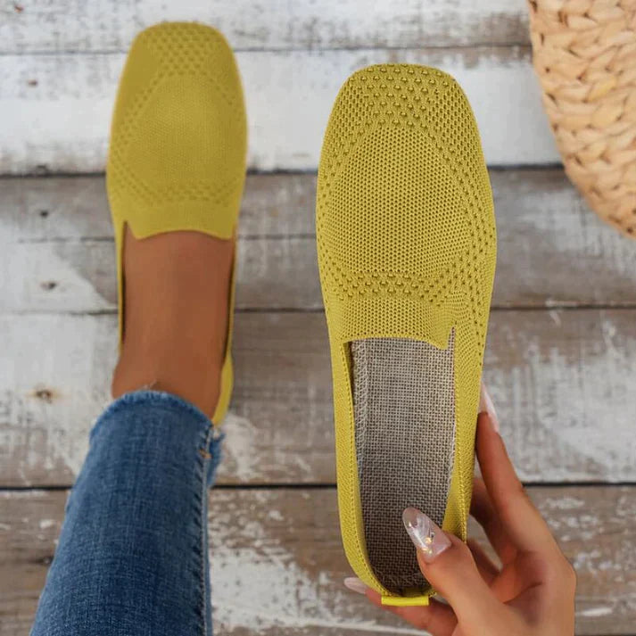 Green slip-on flats with one shoe held beside a foot wearing the matching shoe.