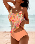 Orange tankini set with patterned top and plain briefs against a pale beach background.