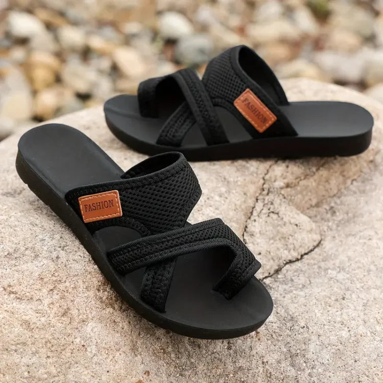 Black slip-on sandals showing broad mesh straps and flat black soles.