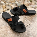 Black slip-on sandals showing broad mesh straps and flat black soles.