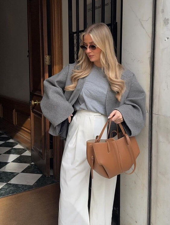 Woman outside a doorway holding a small brown tote by its short handles.