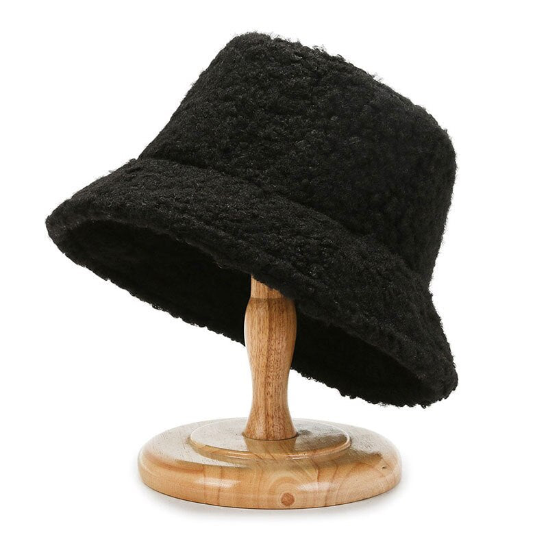 Black curly-textured bucket hat displayed on a wooden stand.