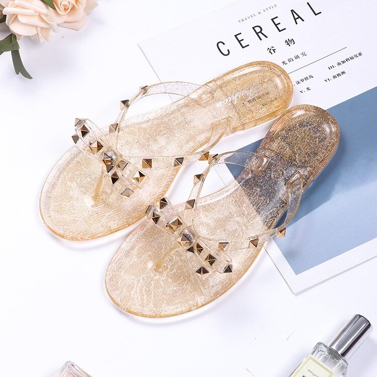Gold-tone sandals with transparent studded straps and decorative bows.