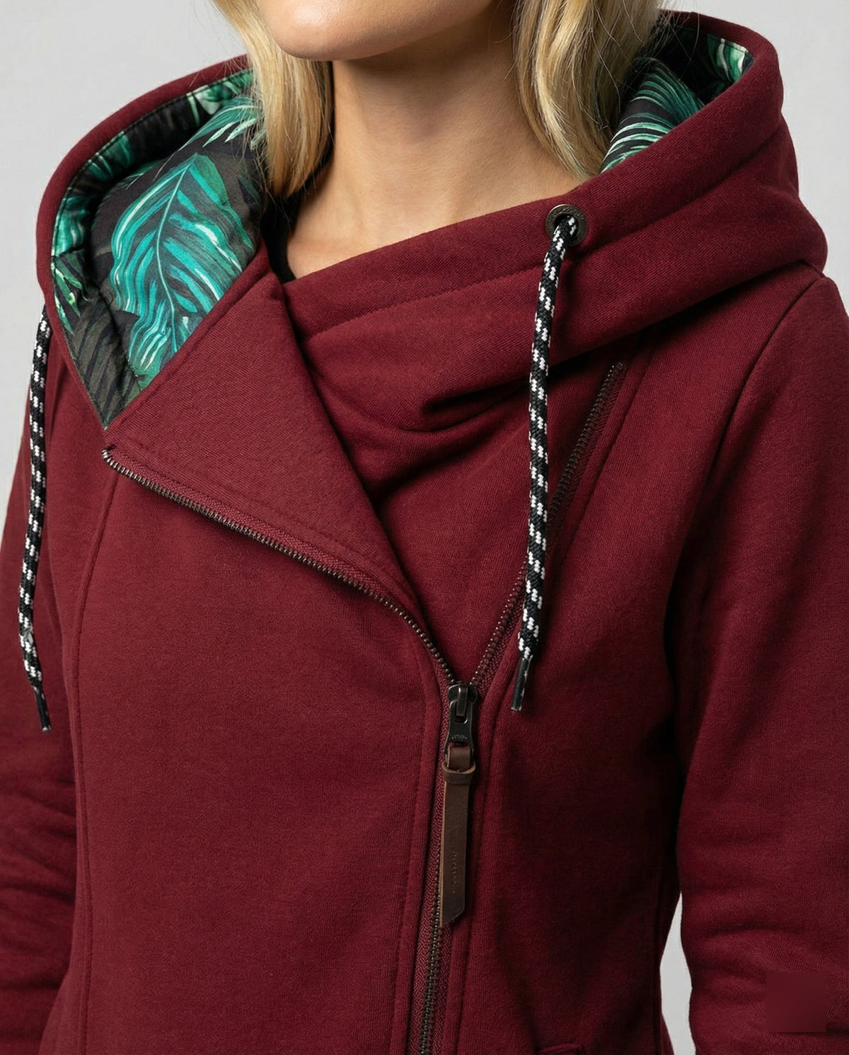 Wine-red coat detail showing a diagonal zip and green leaf-print hood lining.