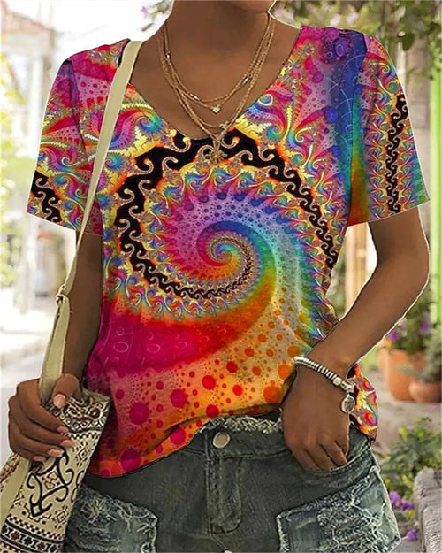 Multicoloured spiral-print T-shirt with a V-neck and short sleeves, worn with denim shorts.