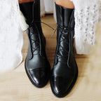 Black lace-up boots with textured shafts and shiny toe caps beside white lace clothing.