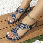 Dark blue floral-cutout sandals with shiny trim, shown on a wooden seat.