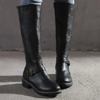Black boots with ankle buckles and low heels, worn with jeans.