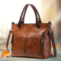 Brown handbag with twin handles, two front pockets and a long strap.