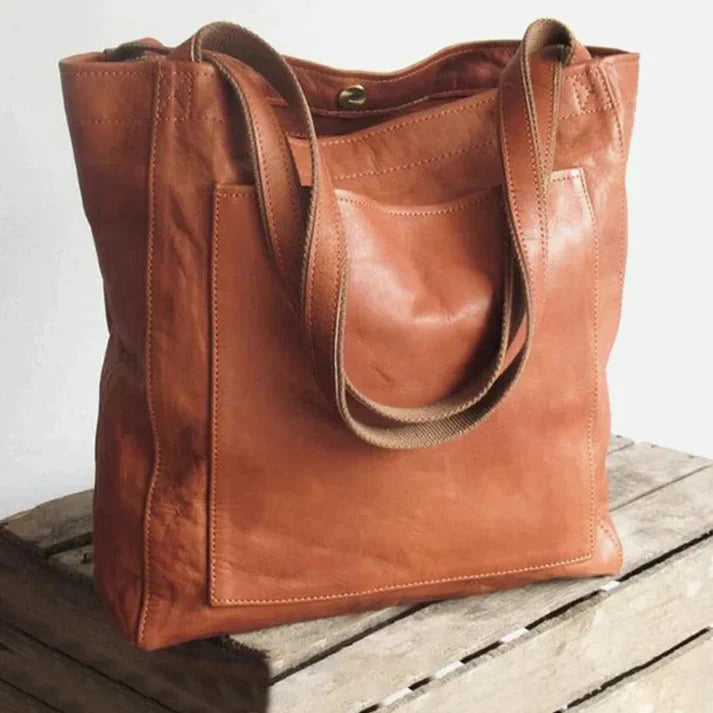 Brown leather tote with twin long handles and a large rectangular front pocket.