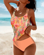 Front view of the multicoloured tankini top and orange briefs beside blue water.