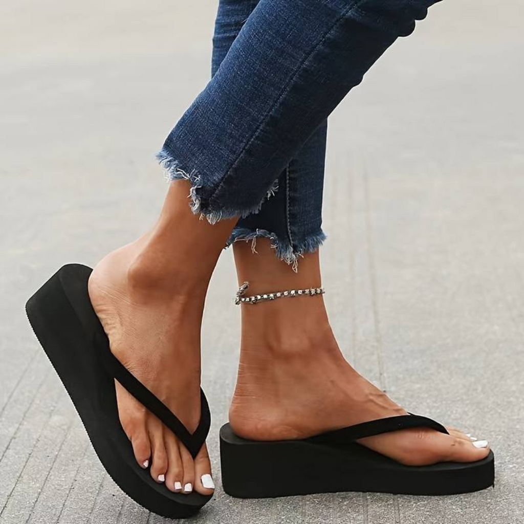 Black toe-post flip-flops with thick platform wedge soles, viewed from the side.