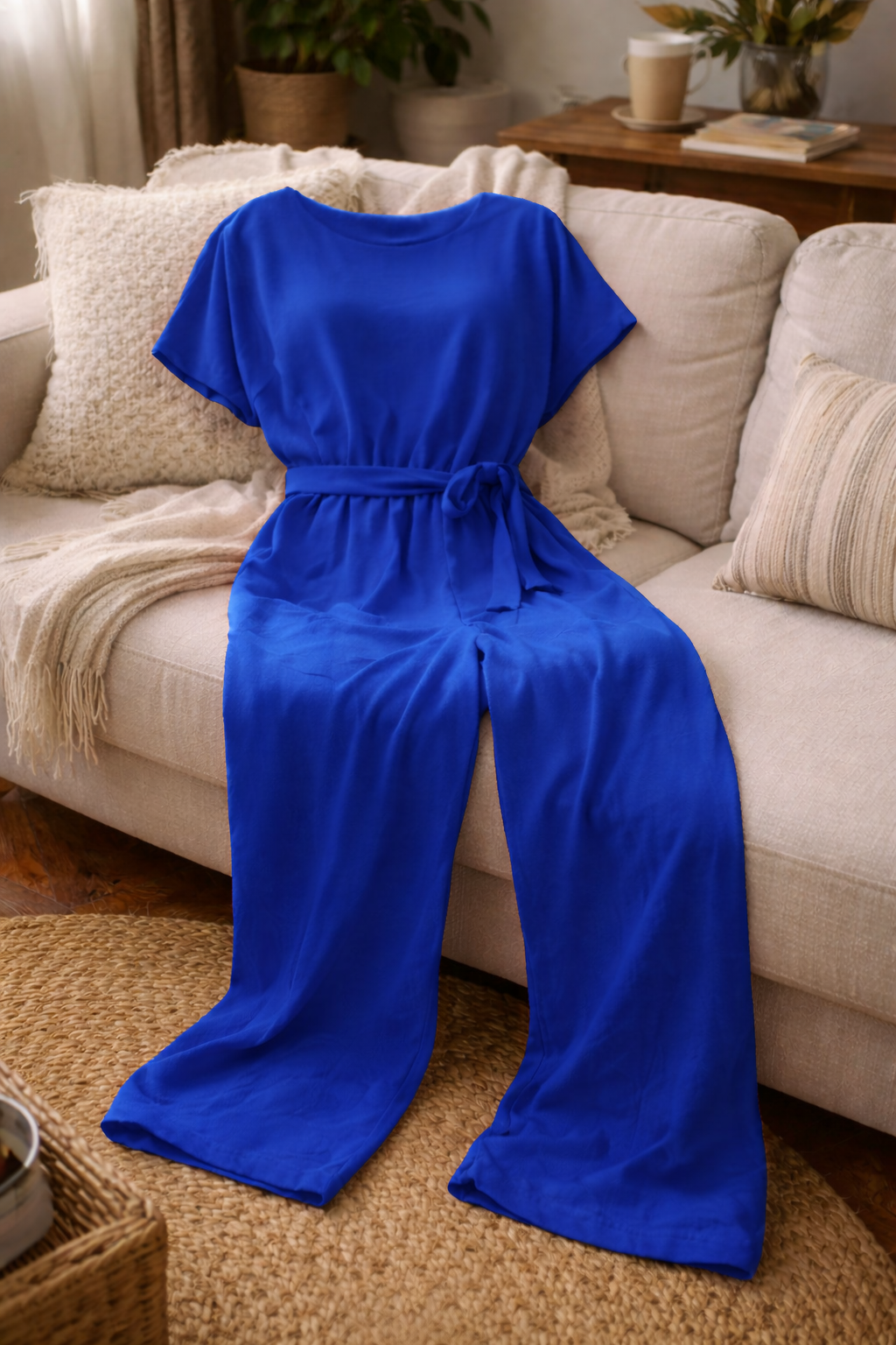 Blue short-sleeve jumpsuit with wide legs, laid out against a cream sofa.