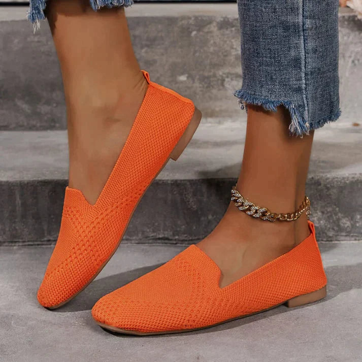 Orange slip-on flats with a low heel, worn with cropped jeans beside steps.