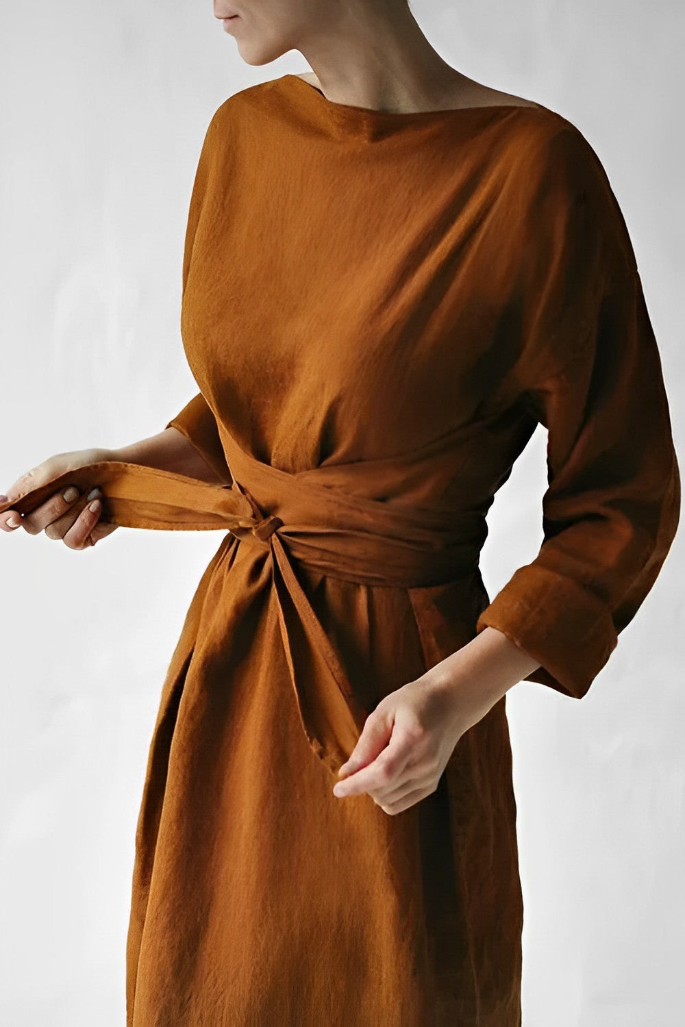 Rust-coloured dress with broad fabric ties wrapped and knotted at the waist.