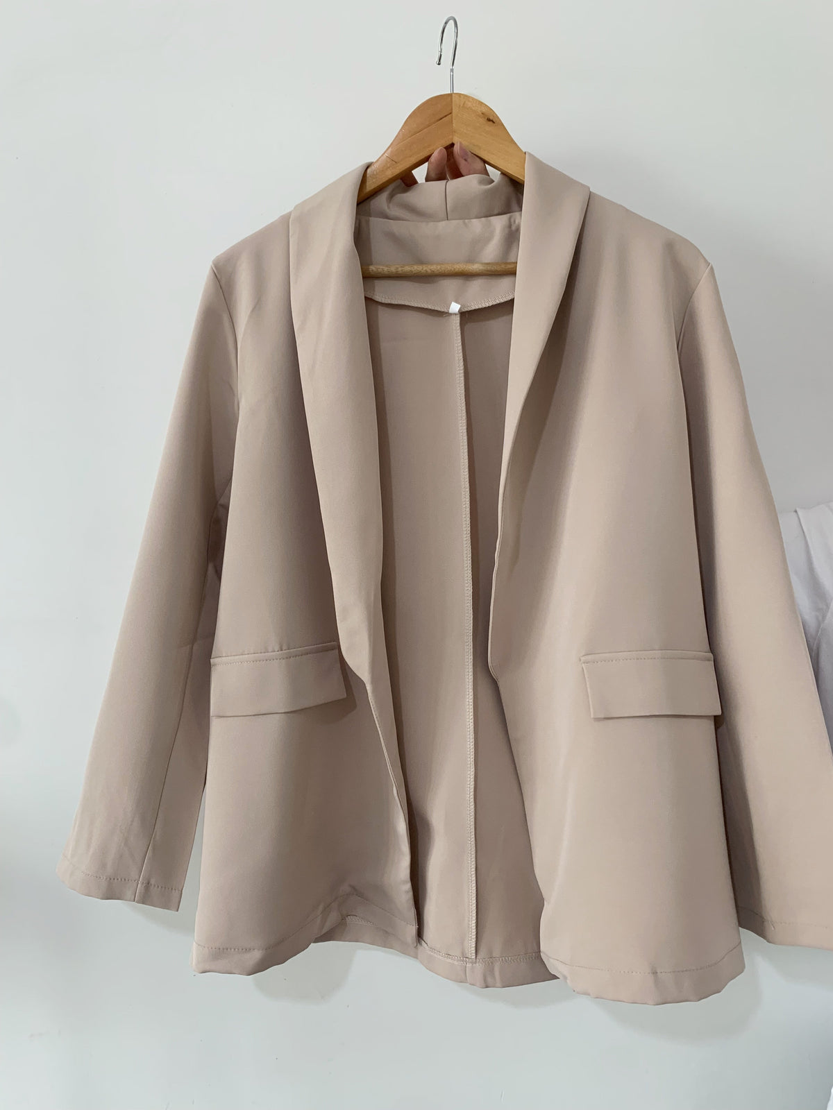Beige long-sleeved blazer on a wooden hanger.